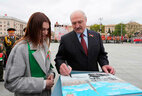 BRSM Youth Union activists show the Belarus president the album “Belarus Remembers” featuring the photos and brief stories about their family members who fought in the Great Patriotic War